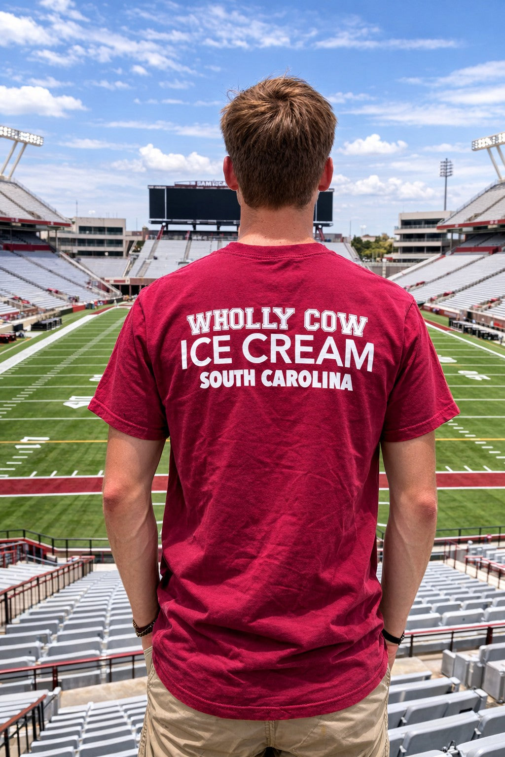 Person wearing a red 'WHOLLY COW ICE CREAM SOUTH CAROLINA' t-shirt at a stadium.