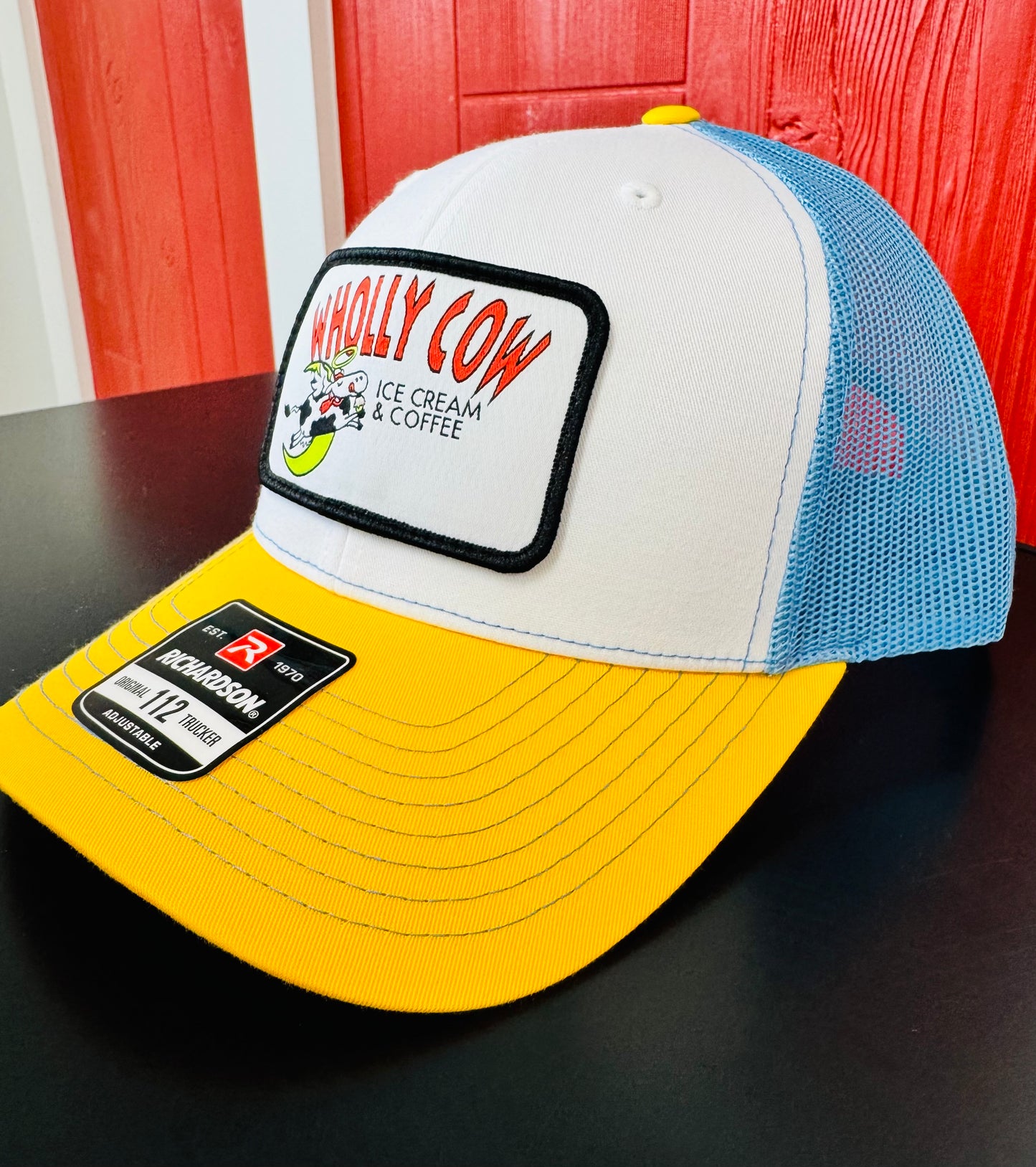 Colorful Richardson trucker cap with a cow logo on a dark surface and red background