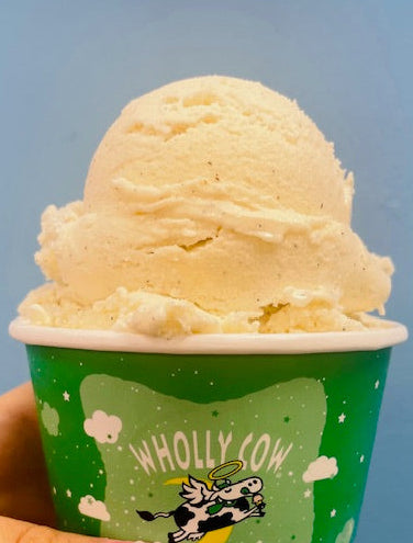 Hand holding a container of Killa Vanilla ice cream Flavor by Wholly Cow Ice Cream with 'Wholly Cow' branding against a blue background