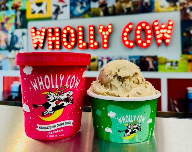 Two containers of Wholly Cow ice cream in front of a sign with the Wholly Cow brand name.