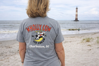 woman wearing a 'Wholly Cow Ice Cream Charleston, SC' t-shirt on a beach with a lighthouse in the background.